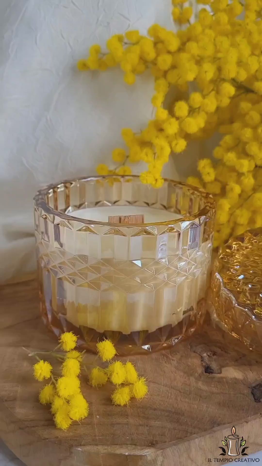 Video della candela in cera di soia con stoppino in legno al profumo di mimosa, realizzata in portagioie di vetro lavorato con coperchio decorato, per celebrare l'8 marzo la Festa della Donna.
